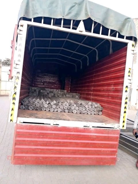 Open-back cargo truck loaded with coiled metal pipes and industrial materials, red and white trailer with navy blue interior