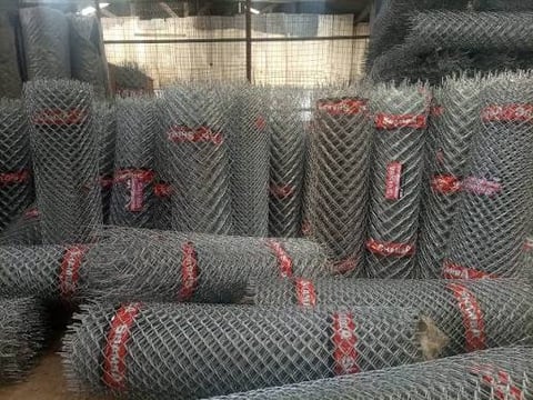 Rolled chain-link fencing coils stacked with red markings in storage yard