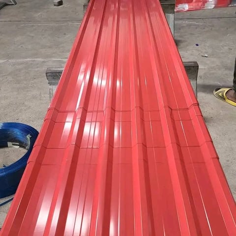 Long red corrugated metal roofing sheet laid on concrete floor in warehouse