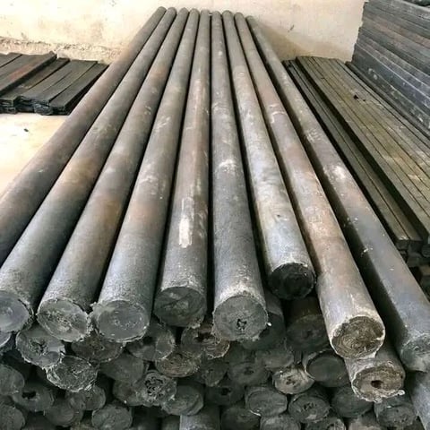 Stack of metal cylindrical pipes arranged in rows on a concrete surface, showing industrial materials storage