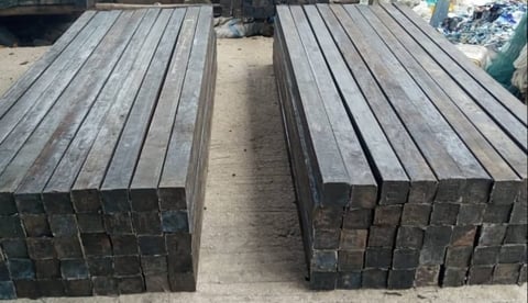 Two rows of stacked wooden railroad ties or timber logs arranged parallel to each other on a concrete surface