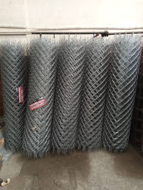 Rolls of galvanized chain-link fence material hanging from a metal rod in an industrial warehouse