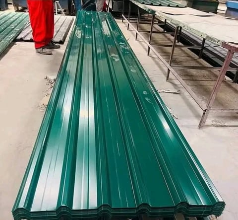 Long green corrugated metal roofing sheet displayed at an industrial warehouse or construction material facility