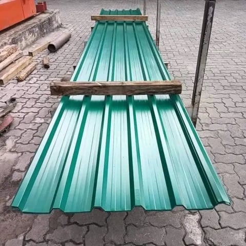 Stacked green corrugated metal roofing sheets on pavement with construction materials nearby